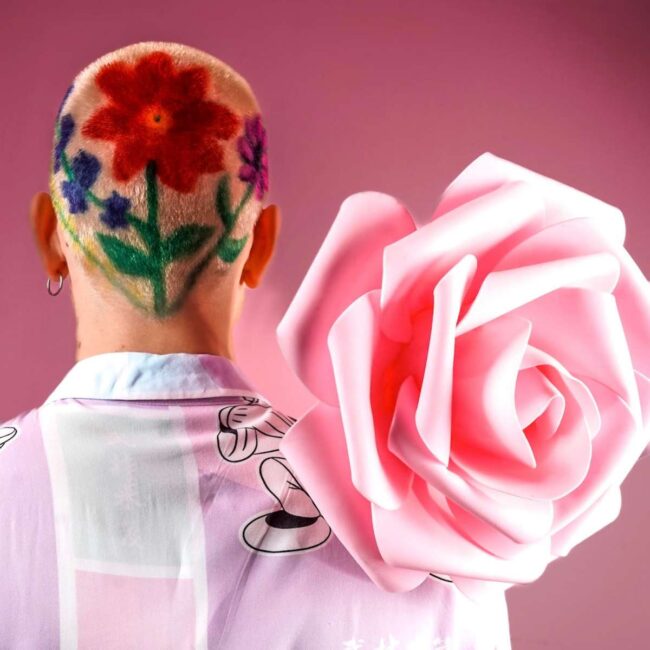 ragazzo di spalle con rosa in mano e con capelli rasati con disegni fiori freehand
